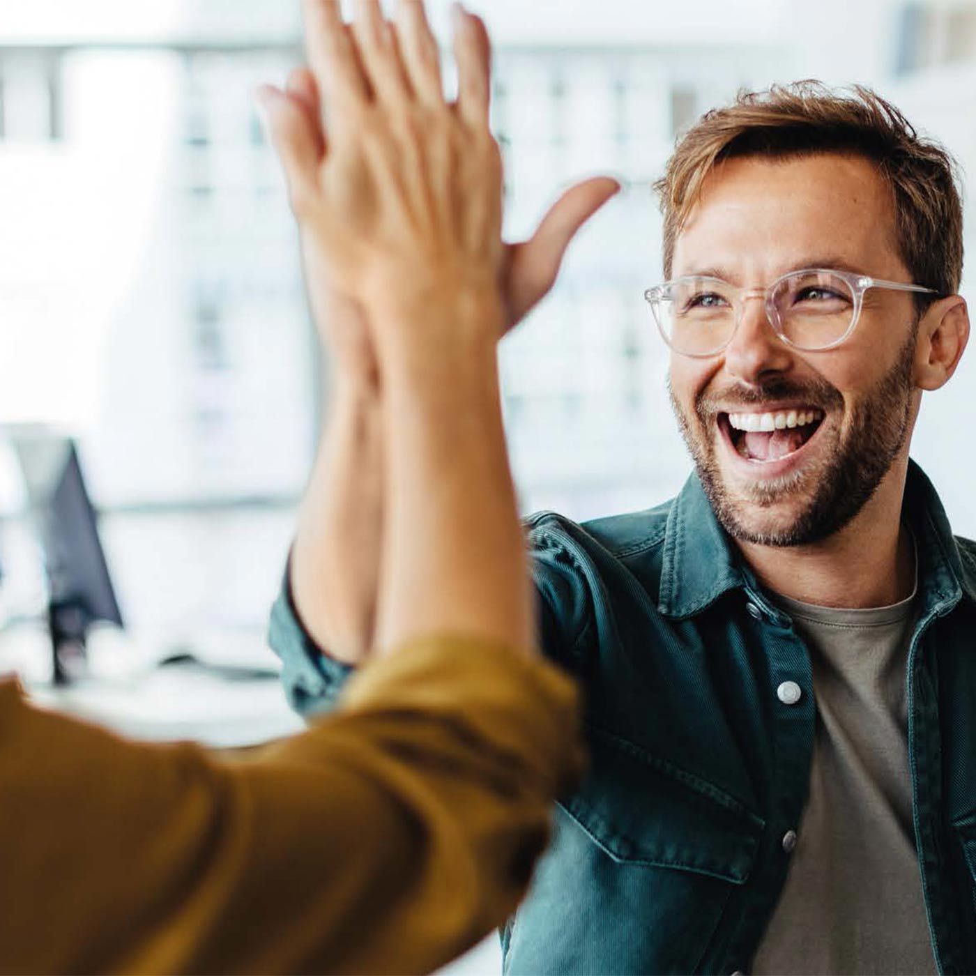 Smiling man with glasses giving a high five to colleague.